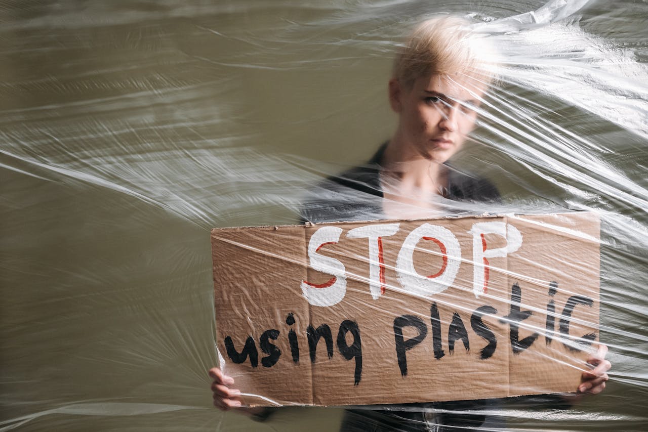 Person holding a sign reading 'Stop using plastic' wrapped in plastic for a protest statement.
